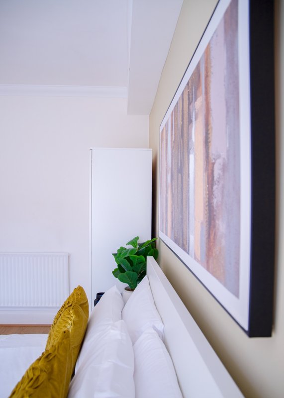 White radiator with potted plant, yellow cushion, and framed artwork on wall