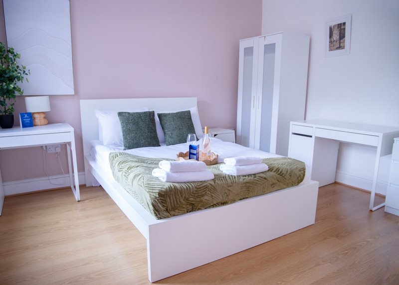 Modern bedroom with pink walls, white bed frame, green bedding, wooden flooring and white furniture