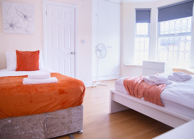 Bright bedroom with two beds, orange bedding, white doors and windows with blinds
