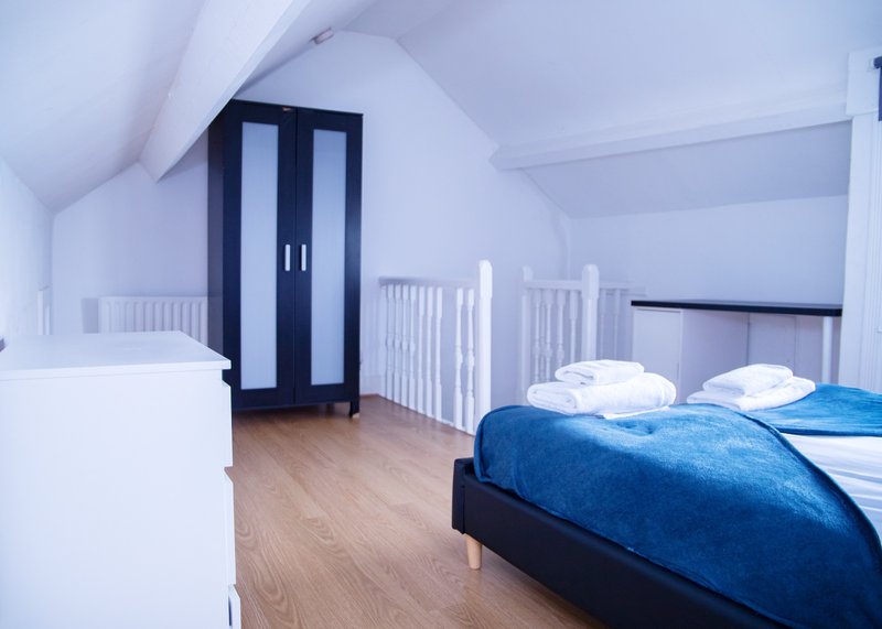 Bright attic bedroom with double bed, blue duvet, white crib, and wooden flooring