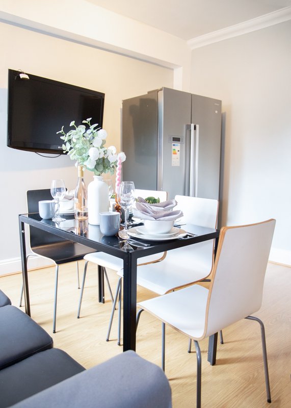 Modern dining area with black table, white chairs, flowers, and wall-mounted TV