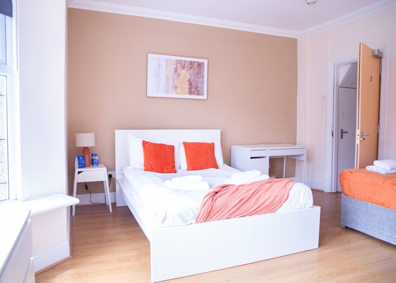 Bright bedroom with white bed, orange cushions, peach walls, wooden floor and bedside furniture