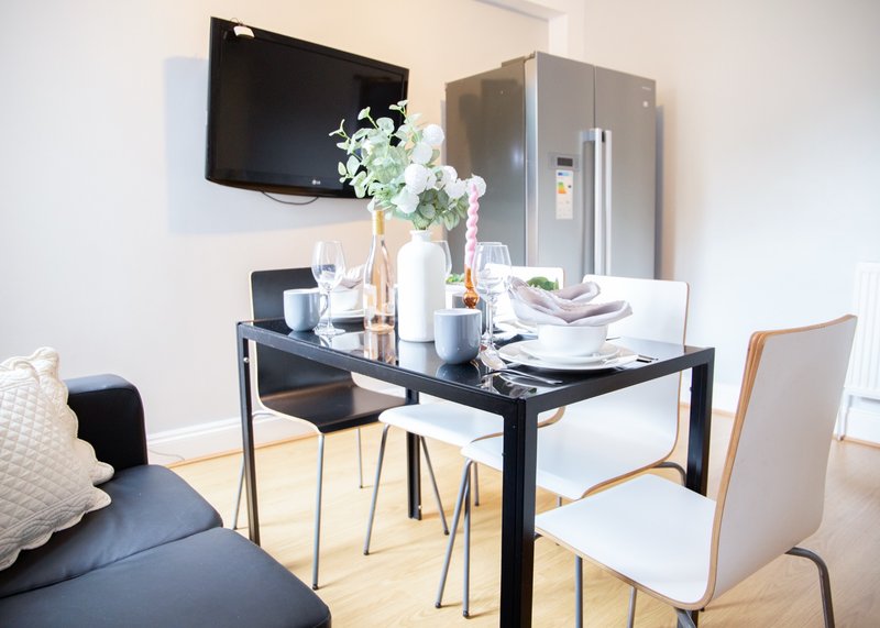 Modern dining area with black table, white chairs, flowers, and wall-mounted television