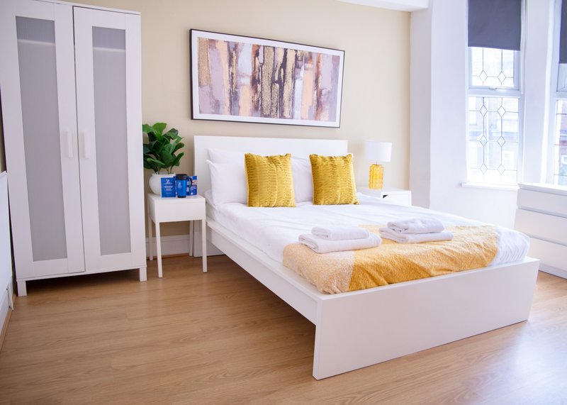 Bright modern bedroom with white bed, yellow cushions, wooden floor and wardrobe