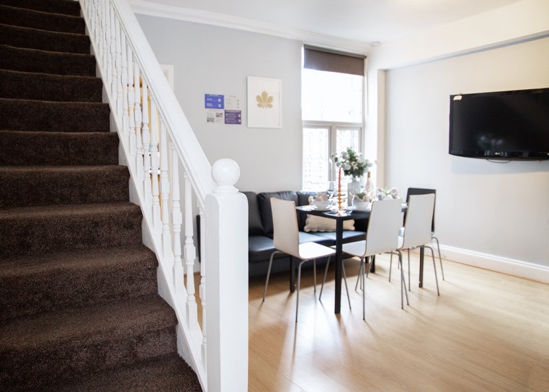 Open-plan living space with staircase, dining table, chairs, and wall-mounted television
