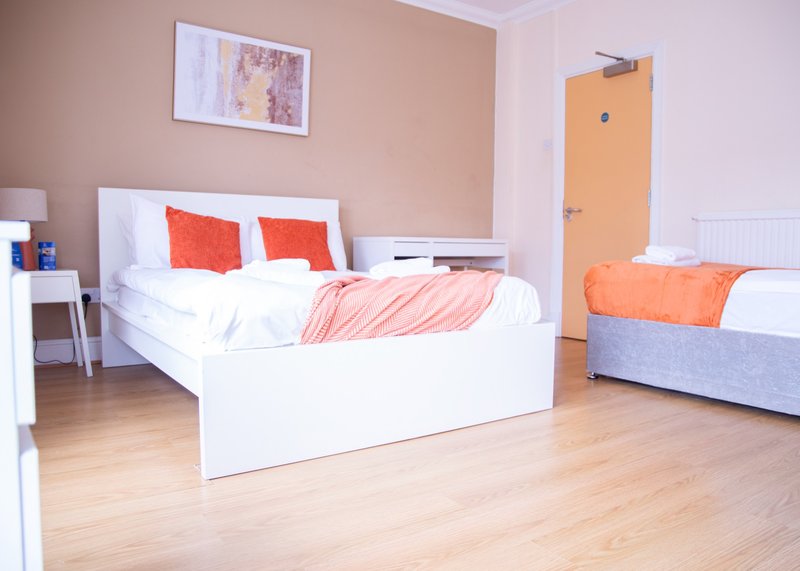 Bedroom with two white beds, red and orange bedding, wooden flooring, and peach-colored walls