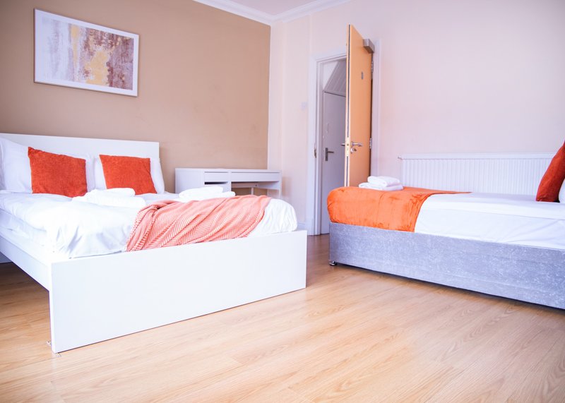 Shared bedroom with two single beds, wooden flooring, orange and red bedding, and wall art