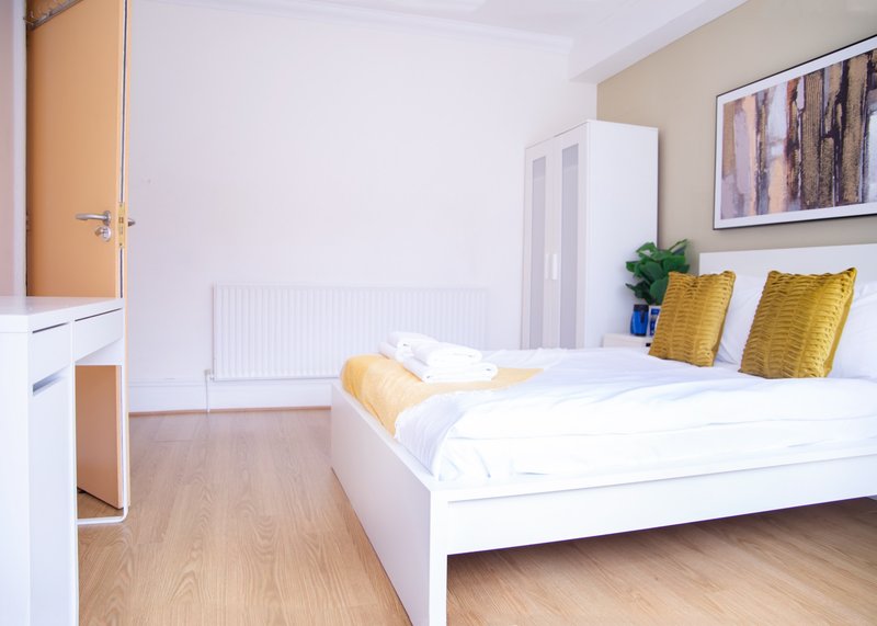 Bright bedroom with white double bed, yellow pillows, wooden floor and wall art