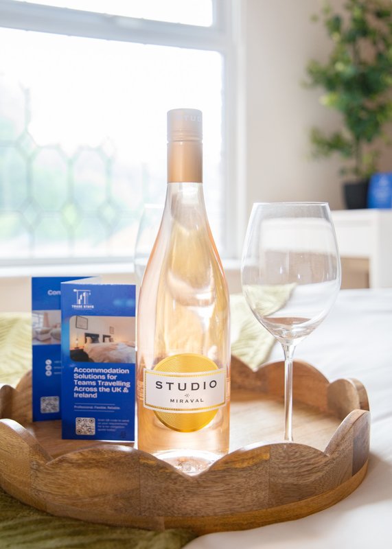 Wooden table styling with wine bottle, glass, and blue accommodation brochure by window