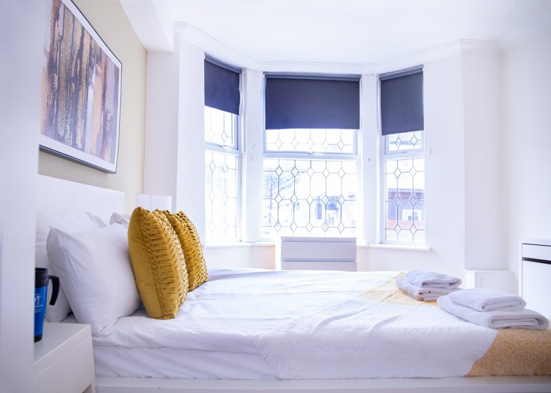 Bright bedroom with double bed, yellow cushions, bay window with navy blinds and street view