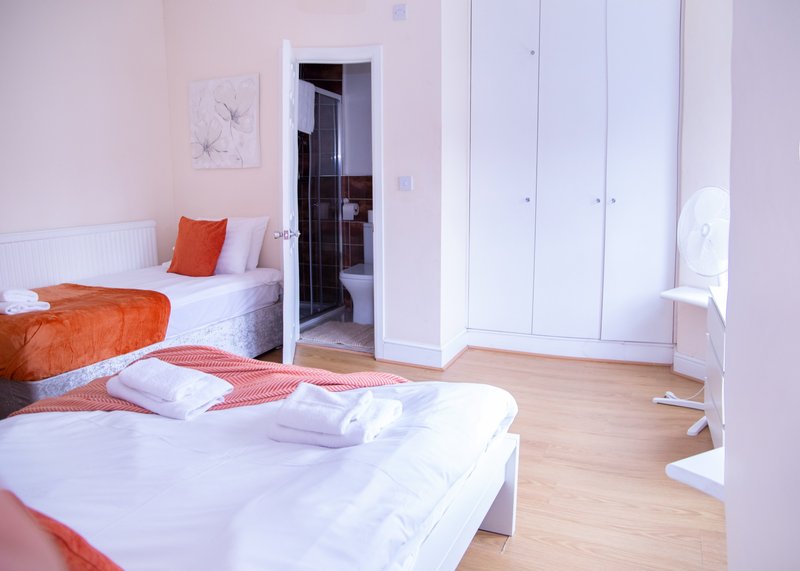 Bright bedroom with two beds, wooden floor, pink walls and white wardrobe