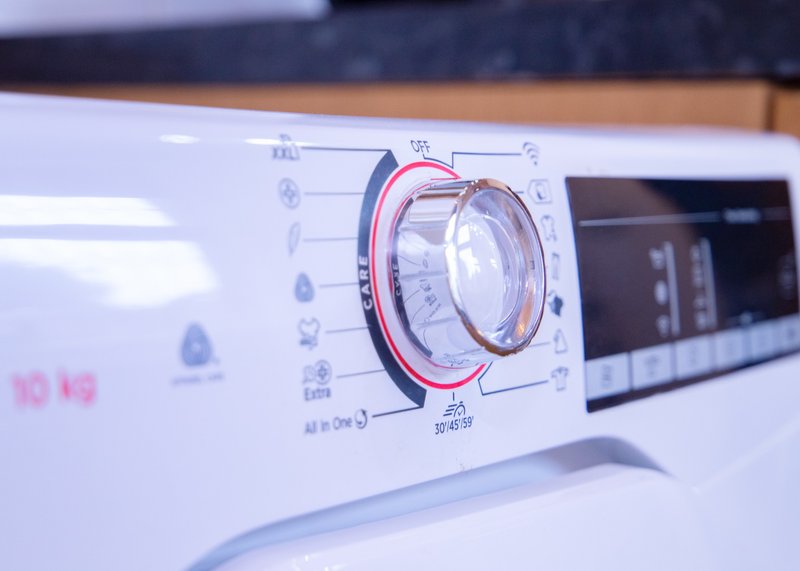 Close-up of white washing machine control panel with dial and digital display