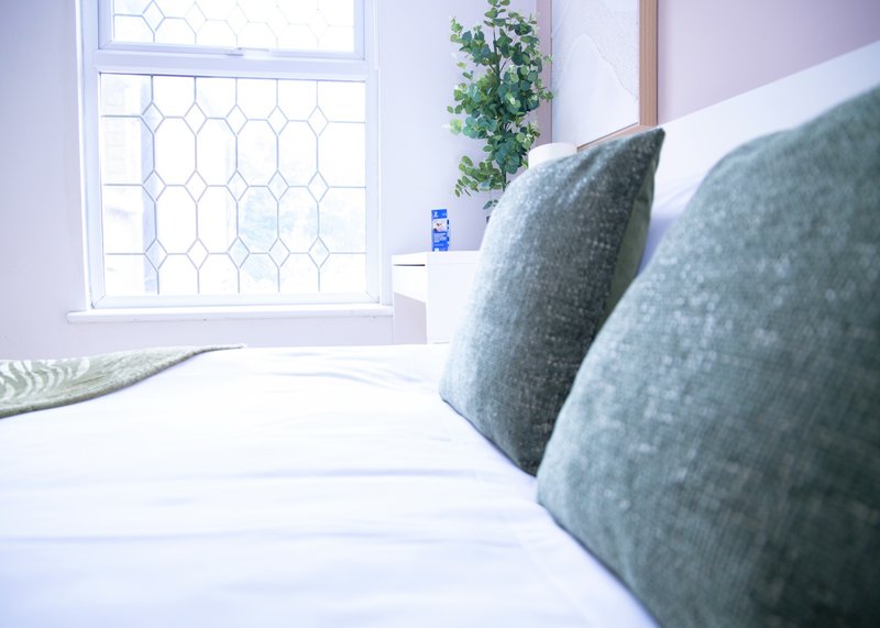 Bright bedroom with double bed, gray cushions, and decorative window with geometric patterning