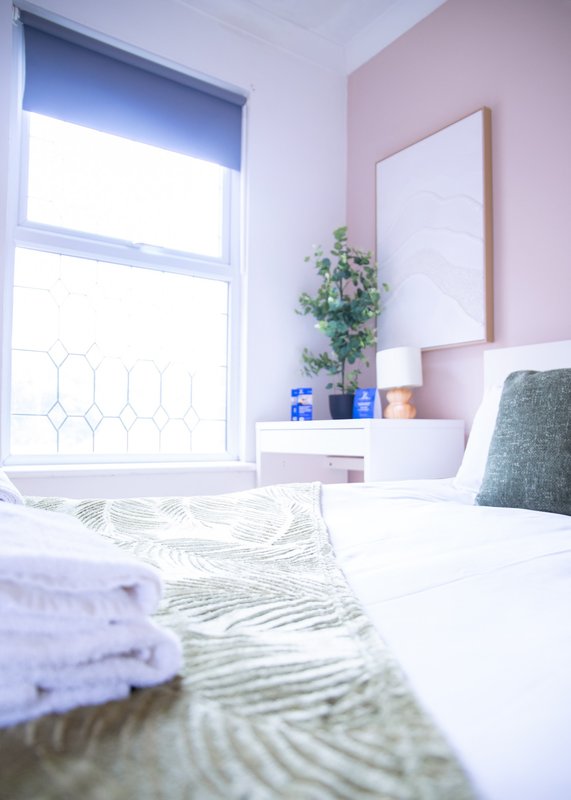 Bright bedroom with double bed, pink accent wall, window, mirror and potted plant