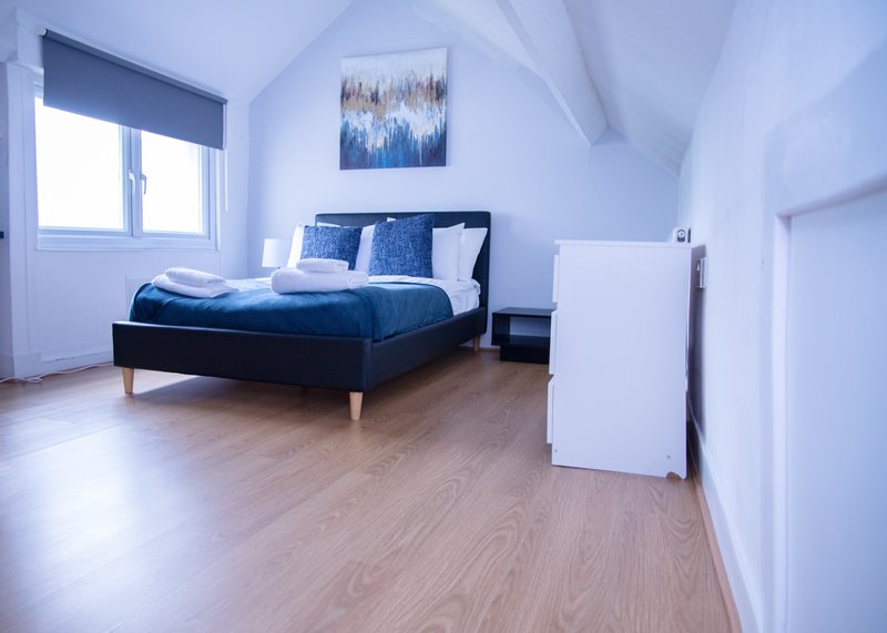 Bright bedroom with double bed, blue bedding, wooden floor and sloped ceiling