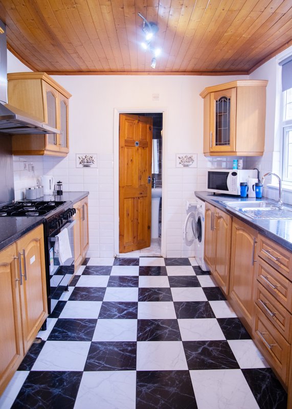 Galley kitchen with wooden cabinets, checkered tile floor, gas cooker and appliances