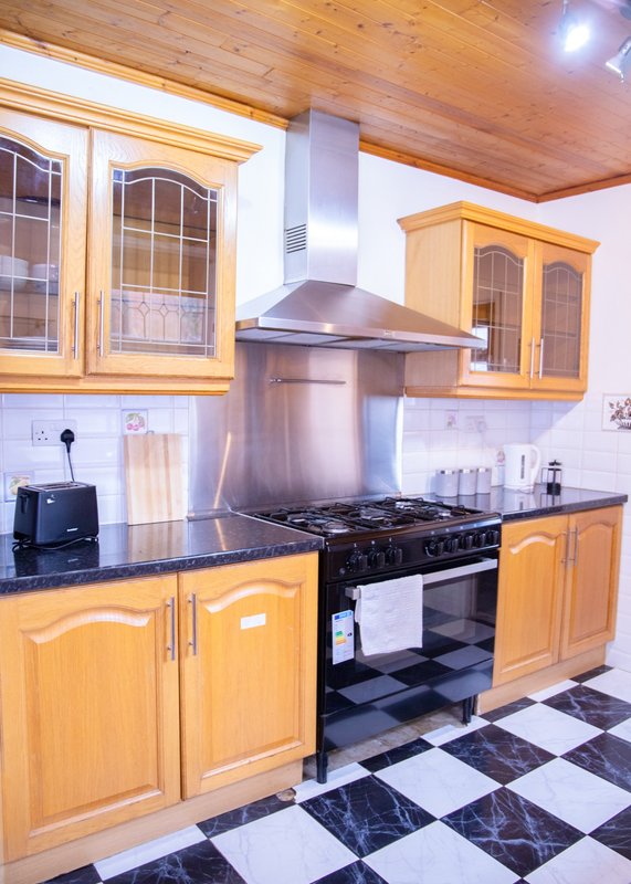 Modern kitchen with wooden cabinets, black range cooker, stainless steel hood and black and white tiled floor