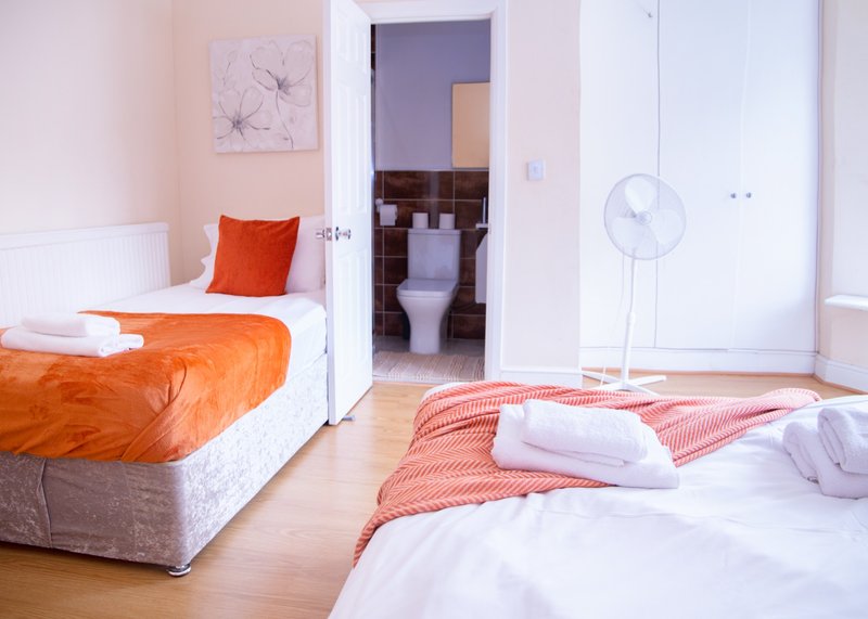 Bright bedroom with two beds, orange bedding, wooden floor and ensuite bathroom visible