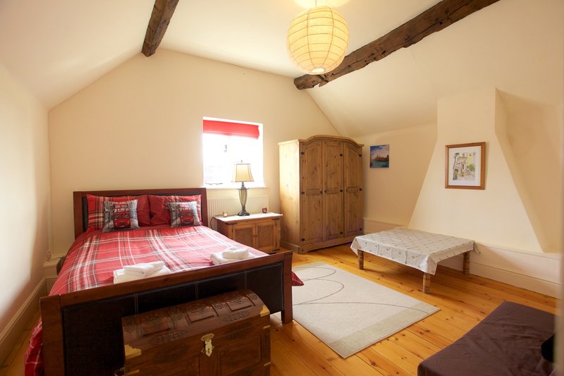 Spacious attic bedroom with double bed, wooden beams, window, and wooden wardrobe