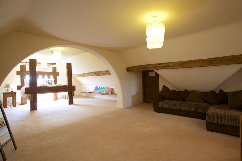 Spacious attic room with sloped ceiling, exposed beams, sofa and shelving unit