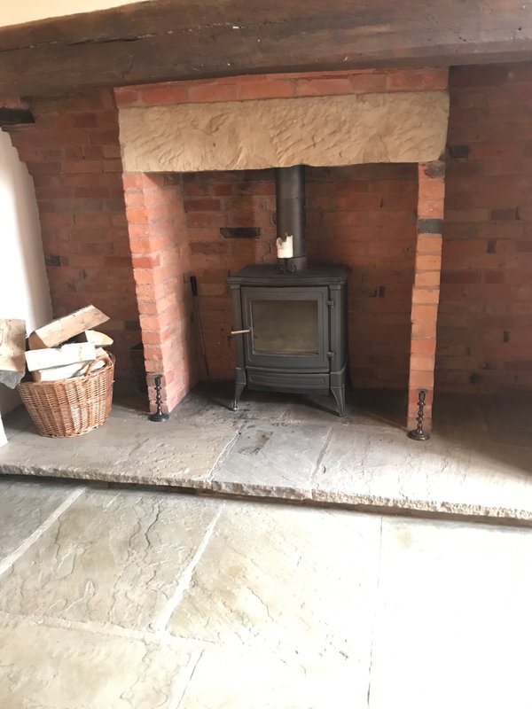 Brick fireplace with black wood stove, cream mantelpiece and wicker basket