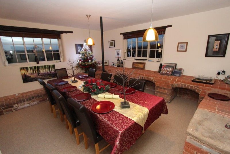 Dining room with long table, burgundy tablecloth, pendant lights, and brick fireplace