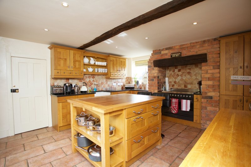 Spacious kitchen with wooden cabinetry, central island, brick fireplace and terracotta floor