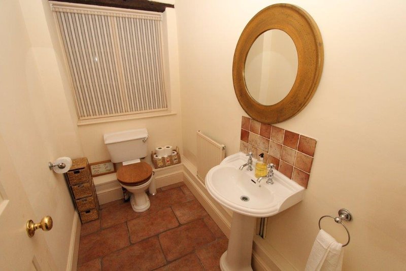 Bathroom with toilet, pedestal sink, round mirror, and terracotta tile flooring