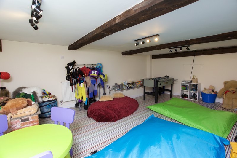 Playroom with exposed wooden beams, colorful foam mats, storage bins, and children's toys and clothing