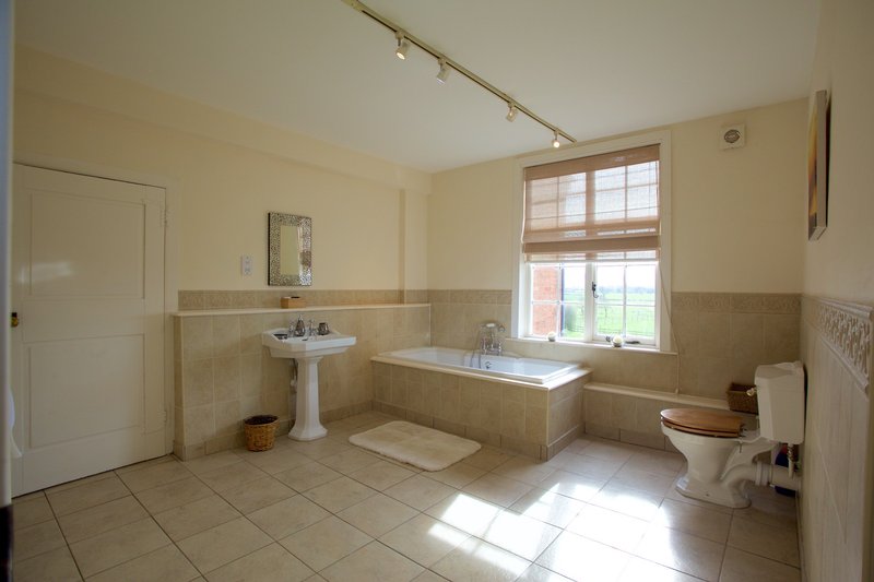 Spacious bathroom with bathtub, pedestal sink, toilet, and large window
