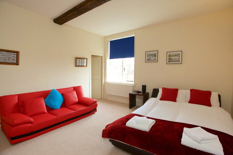 Bright bedroom with red sofa, double bed, blue cushion and exposed wooden beam