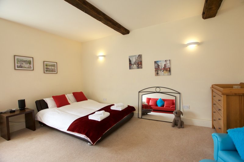 Spacious bedroom with double bed, exposed beams, framed wall art, and colorful cushions