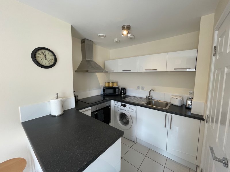Modern kitchen with white cabinets, black countertop, integrated appliances and wall clock