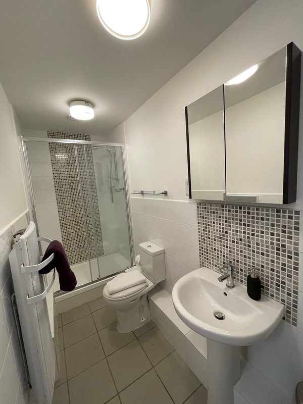 Modern bathroom with shower enclosure, white sink, toilet, and mosaic tile backsplash