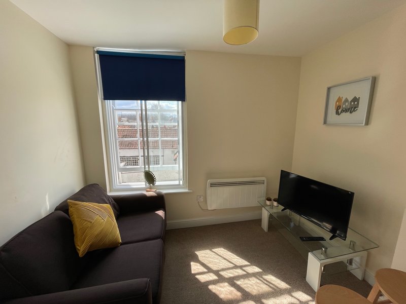 Compact living room with dark sofa, TV stand, window with navy blind, and radiator