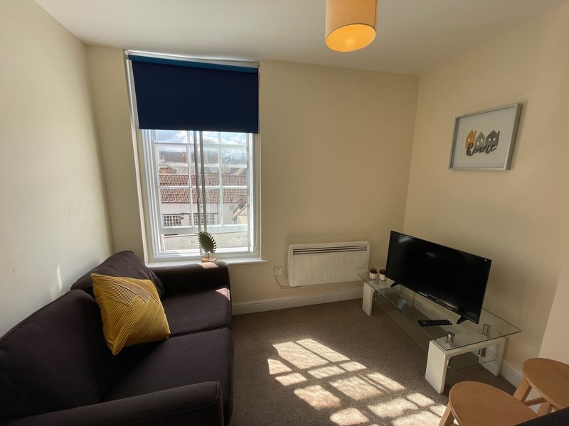 Compact living room with dark sofa, TV stand, window with blind and city view