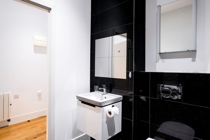 Modern bathroom with black tile wall, white sink, mirror and wooden flooring