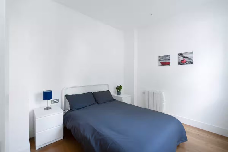 Minimalist bedroom with double bed, dark blue bedding, white nightstand and radiator