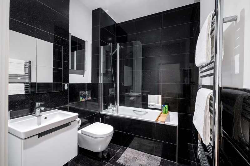 Modern bathroom with black tile walls, white sink, toilet, walk-in shower and towel rail