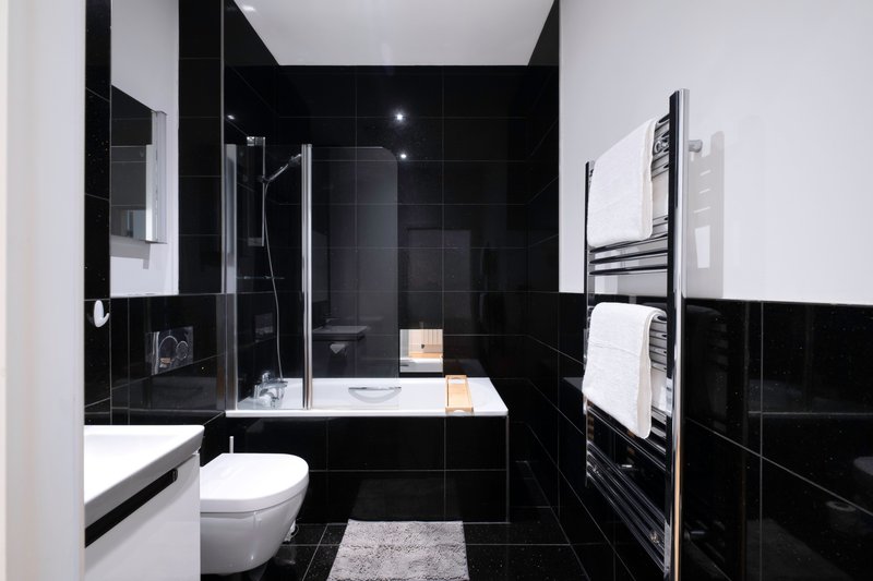 Modern bathroom with black tile walls, white toilet, glass shower enclosure and heated towel rail
