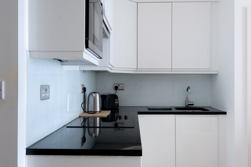 Modern white kitchen with black countertop, kettle, microwave and integrated appliances
