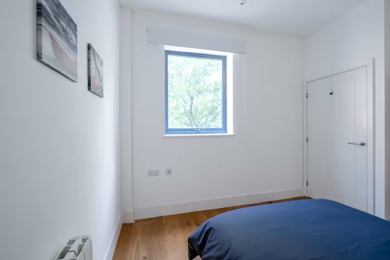 Bright bedroom with blue bed, wooden floor, window, and wall art