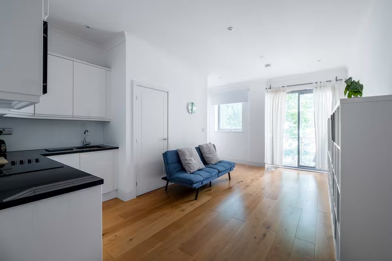 Modern open-plan kitchen and living area with wooden floors, blue sofa, and glass doors to garden