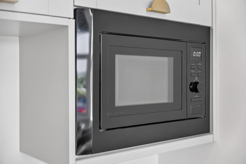 Built-in black microwave oven in white kitchen cabinet with brass handle