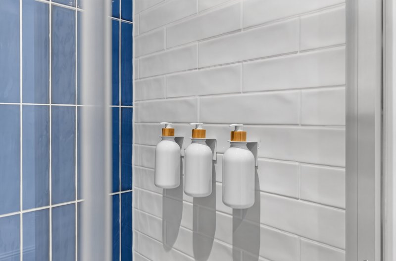 Modern bathroom with white subway tile wall, blue tiled shower area, and three white toiletry bottles with amber dispensers