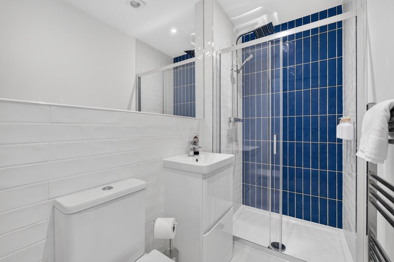Modern bathroom with white subway tile walls, blue tiled shower enclosure and white fixtures