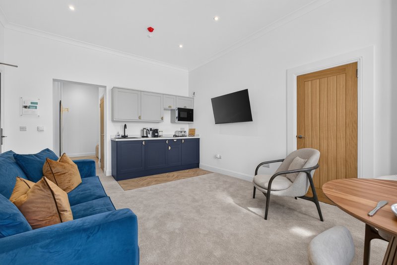 Open-plan living area with blue sofa, kitchenette, wall-mounted TV and wooden doors