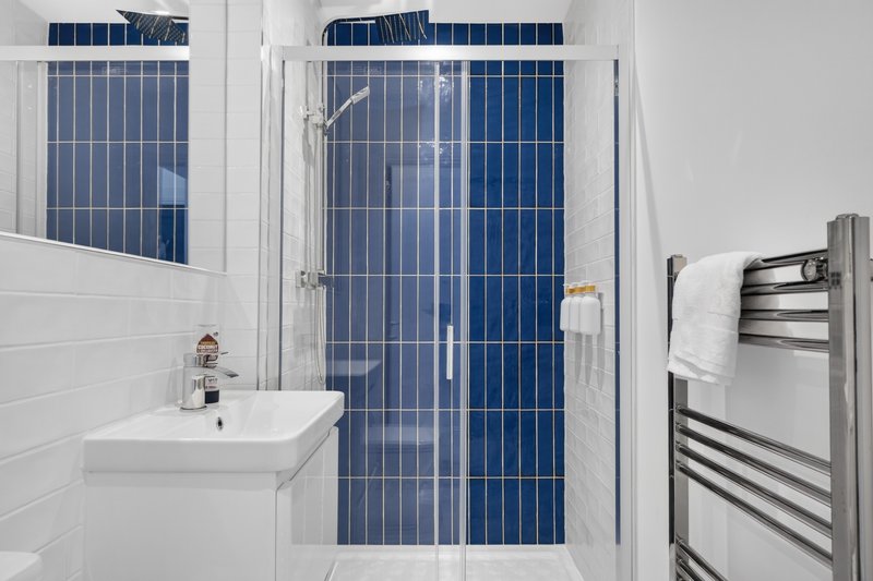 Modern bathroom with white subway tiles, wall-mounted sink, shower enclosure with blue tile wall and towel rail