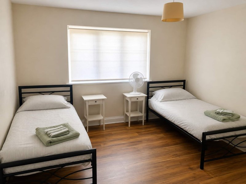 Bedroom with two single beds, wooden floor, white bedside tables and window