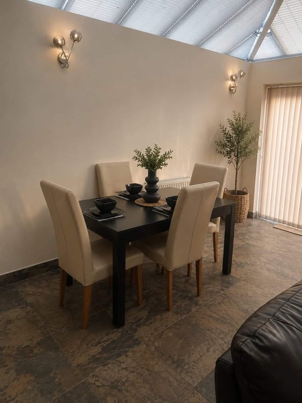 Modern dining area with black table, four beige chairs, potted plants and wall sconces